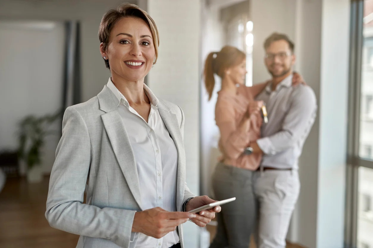 portrait-of-happy-real-estate-agent-with-a-couple-in-the-background.webp