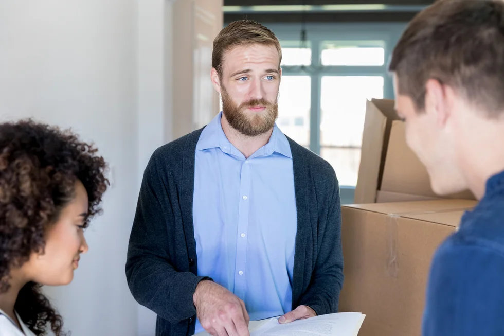 serious-male-real-estate-agent-discusses-paperwork-with-a-couple-who-are-buying-their-first-home.webp