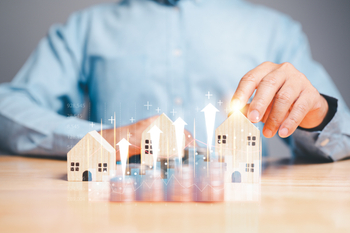 A man in a suit holding a miniature house model in his hand
