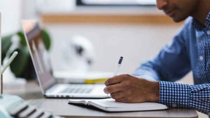 men writing on a notebook next to a laptop