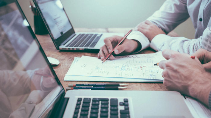 table with multiple notebooks and two people writing on sheets calculating something