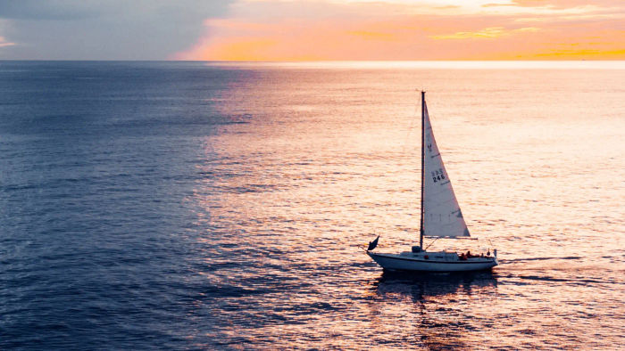 um barco a vela navegando com um por do sol ao fundo