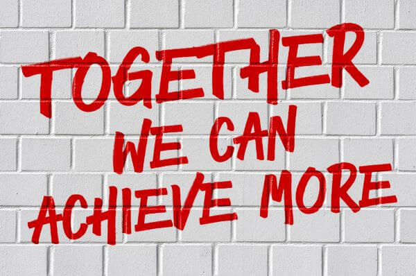 Writing on a white brick wall that says "Together We Can Achieve More"