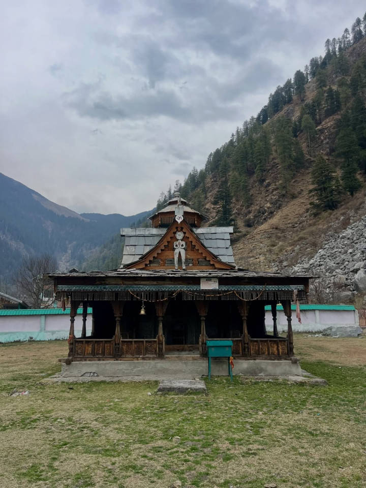 A wooden temple with a tiered roof on a village green in the Kullu valley