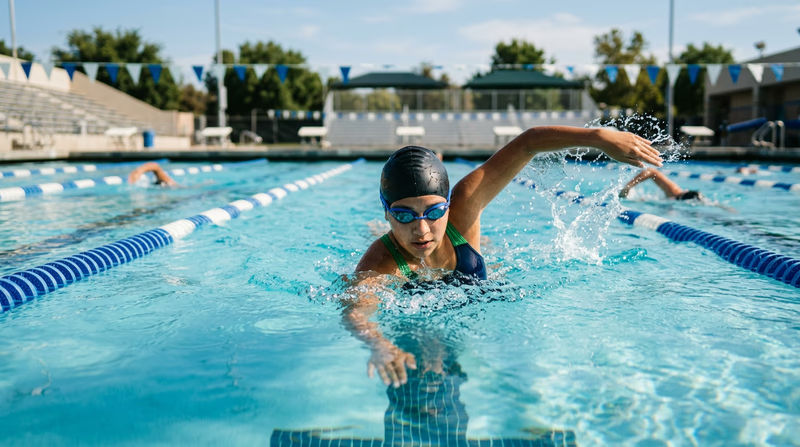 A swimmer doing freestyle in a lane of an outdoor pool, with water splashing cleanly and lane ropes visible