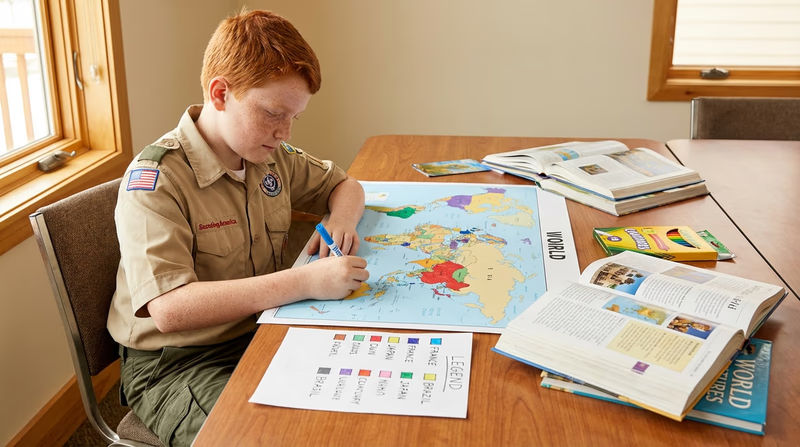 A Scout working on a world map poster at a table, coloring in countries with different markers and creating a legend