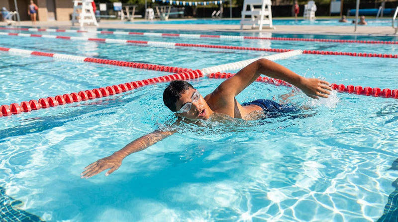 A Scout in a swimming pool, mid-stroke, with clear blue water and lane lines visible
