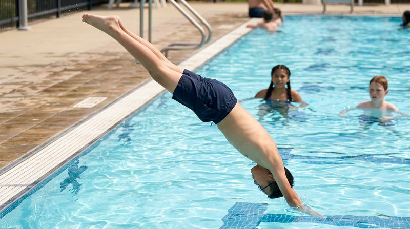 A Scout performing a pike surface dive in a pool, body bent at the waist with legs pointing straight up as they descend headfirst into the water