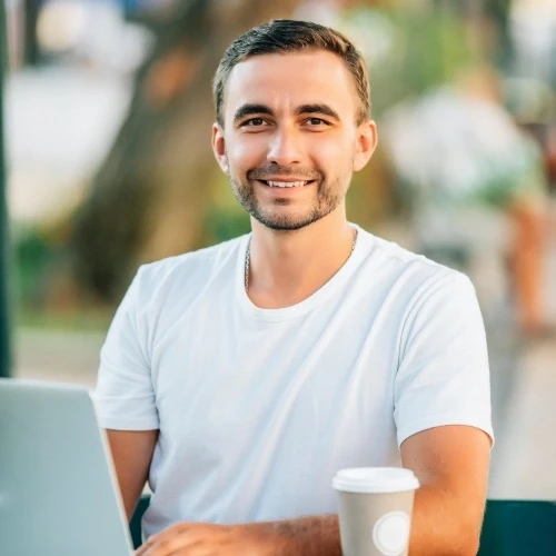 man with white t-shirt sitting in front of laptop and coffee on table