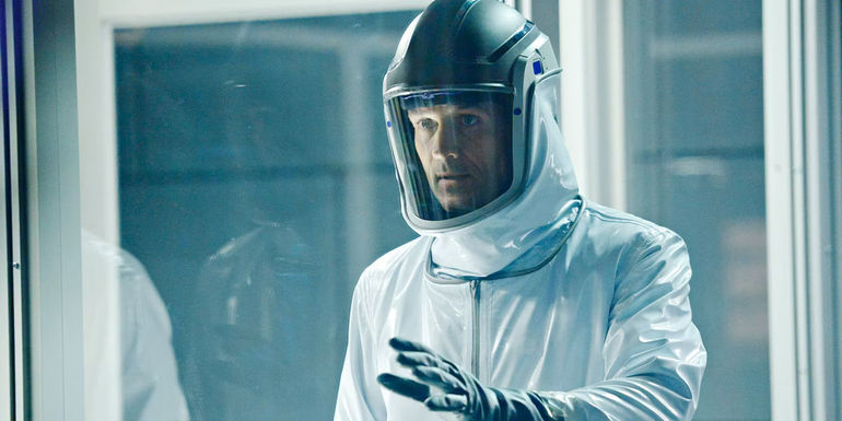 A man in a protective suit with his hand up to a pane of glass in a scene from Helix.