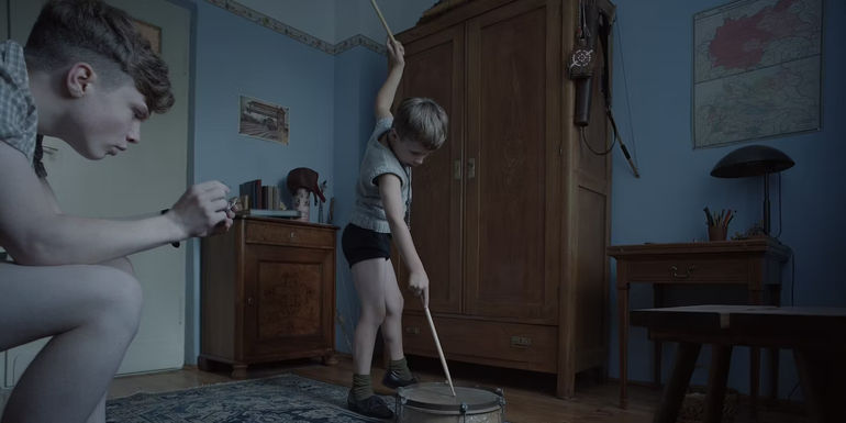 a young boy plays the drum in the zone of interest
