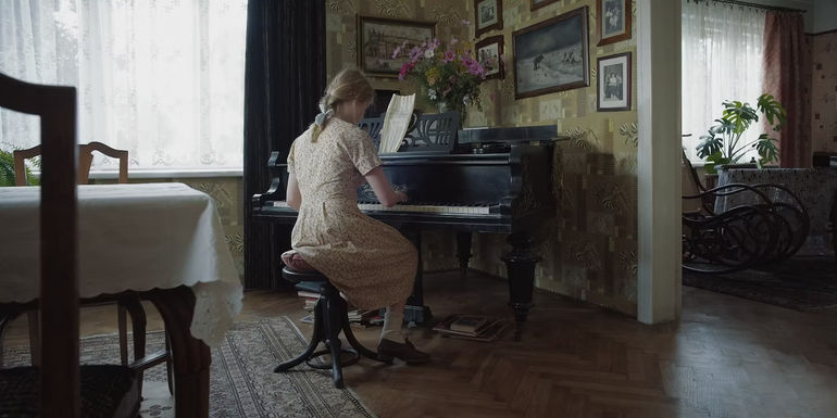 a woman plays the piano in the zone of interest