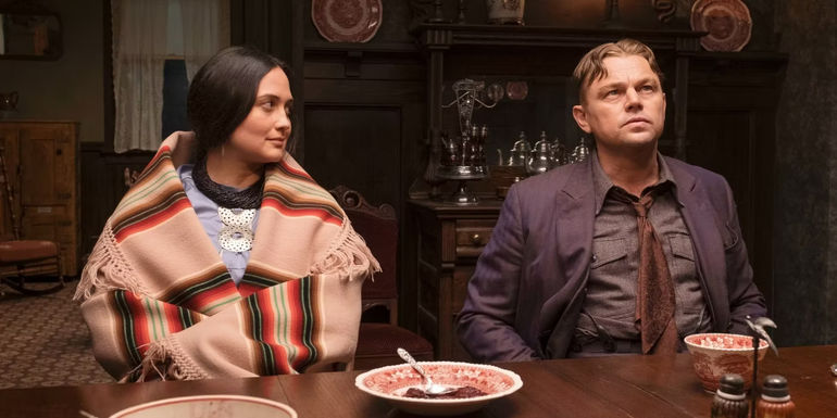 Leonardo DiCaprio as Ernest Burkhart and Lily Gladstone as Mollie Burkhart sitting at a table in Killers of the Flower Moon