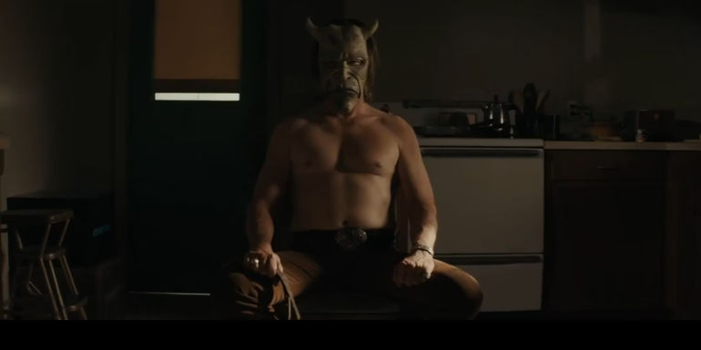 The Grabber (Ethan Hawke) sitting shirtless in a dark room in The Black Phone.