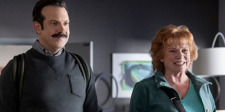 Ted Lasso (Jason Sudeikis) and Dottie Lasso (Becky Ann Baker) smiling in Rebecca's office in 