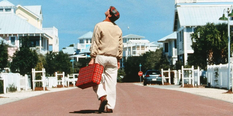 Jim Carrey as Truman Burbank looks up at the artificial sky while walking down a long road in The Truman Show.
