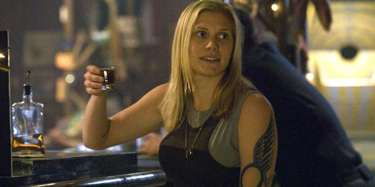 Starbuck raises a shot glass into the air while sitting at a bar.