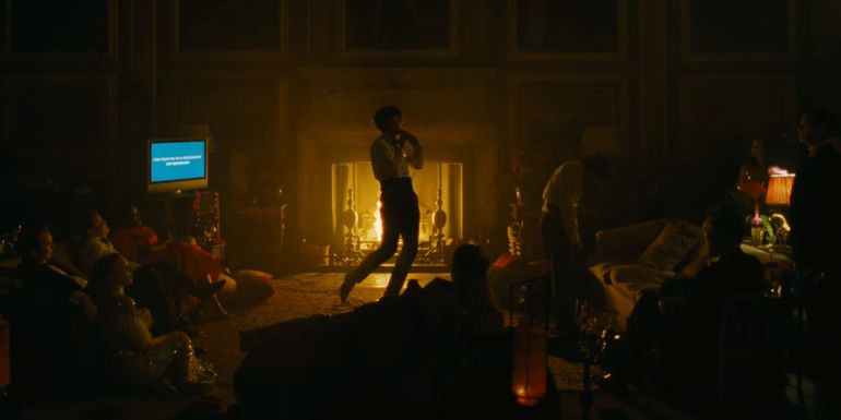 Farleigh (Archie Madekwe) singing karaoke in front of the fireplace at a party in Saltburn.