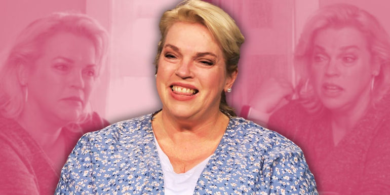 janelle brown in blue top smling pink background