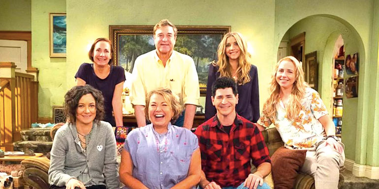 Sara Gilbert's Darlene, Laurie Metcalf's Jackie, John Goodman's Dan, Roseanne Barr's Roseanne, Sarah Chalke's Andrea, Michael Fishman's DJ, and Lecy Goranson's Becky pose by a couch in a Roseanne season 10 promo photo
