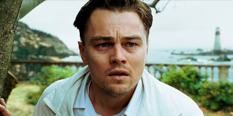 Leonardo DiCaprio as Teddy Daniels looking concerned with a lighthouse behind him in Shutter Island.
