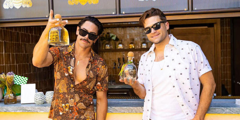 Vanderpump Rules' Tom Sandoval and Tom Schwartz wear sunglasses while smiling with bottles of Patron tequila in their right hand. 