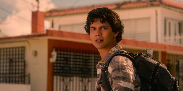 Miguel standing in Mexico with a backpack, looking at something in a scene from Cobra Kai.