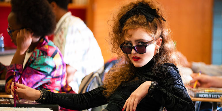 Kathryn Newton as Lisa Swallows sitting in a school desk wearing sunglasses and having an attitude in Lisa Frankenstein
