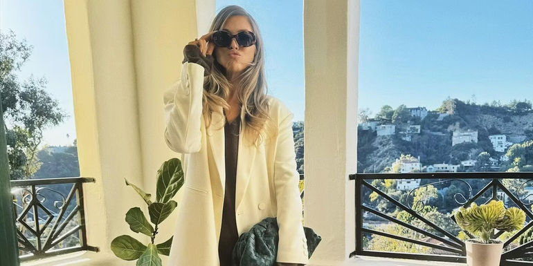 Stassi Schroeder from Vanderpump Rules poses in front of a mountain backdrop and makes a kissy face to camera while wearing sunglasses.