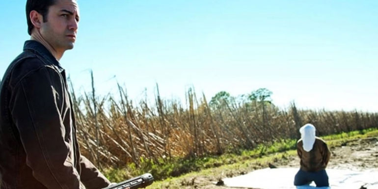 Jason Gordon-Levitt as Young Joe aiming his weapon at a hooded figure on his knees in Looper