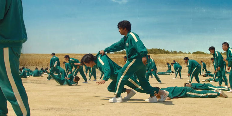 Ali holds Gi-hun up as he's falling in Red Light Green Light in Squid Game.