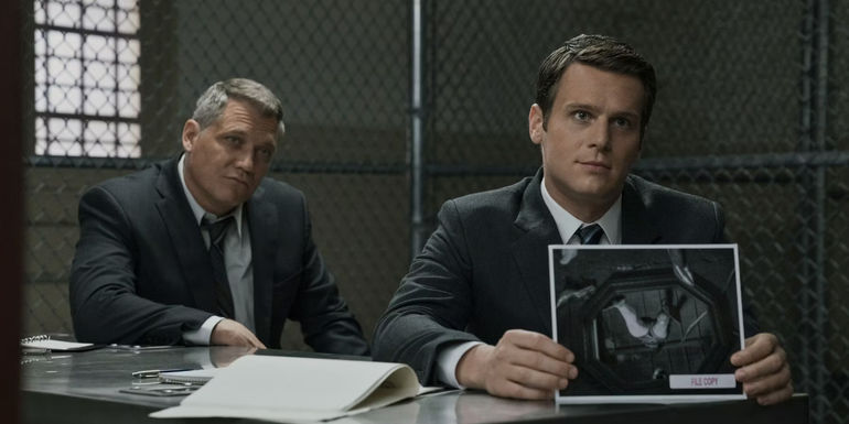 One man holds a picture of a dead body as the other looks on in Mindhunter.