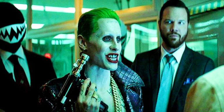Joker holds a tool while talking to someone and flanked by guards in Suicide Squad