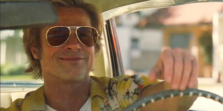 Cliff Booth (Brad Pitt) smiling while wearing sunglasses and driving his car in Once Upon A Time... in Hollywood.