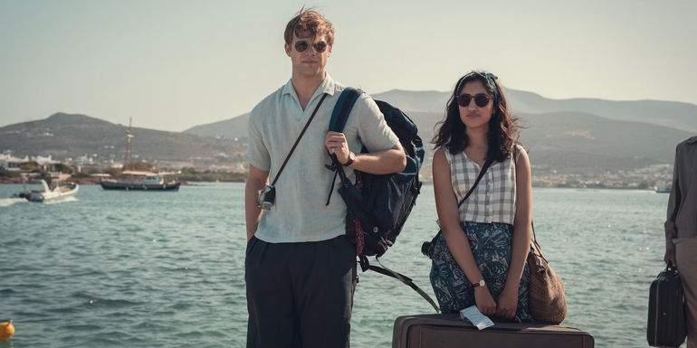 Dexter and Emma stand on a dock on vacation with their luggage in One Day