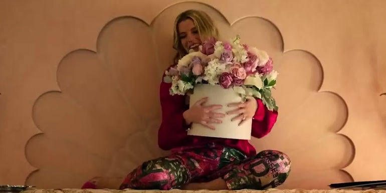 Amelia sitting on the shelf holding flowers in Roar