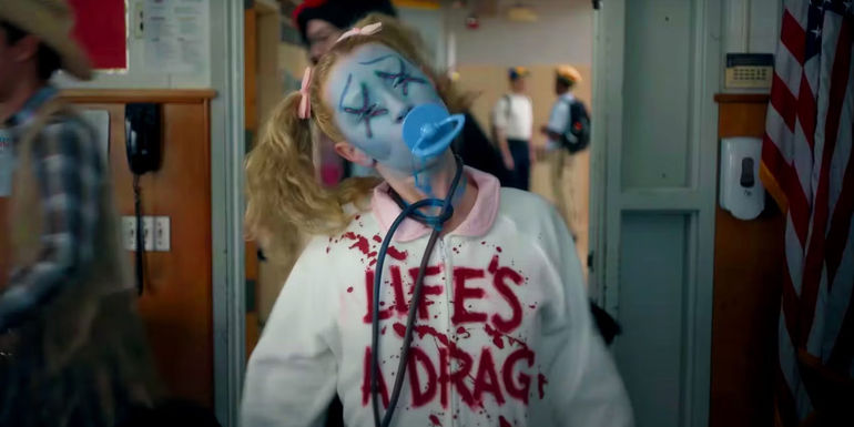 Women in pigtails and a pacifier in her mouth wearing a white hooding with Lifes A Drag written on it in blood in American Horror Stories season 3 trailer