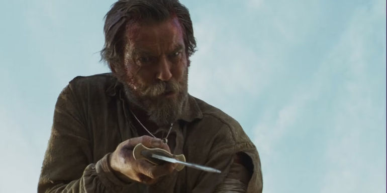 Gideon (Pierce Brosnan) pointing a knife at and standing over Carver in Seraphim Falls