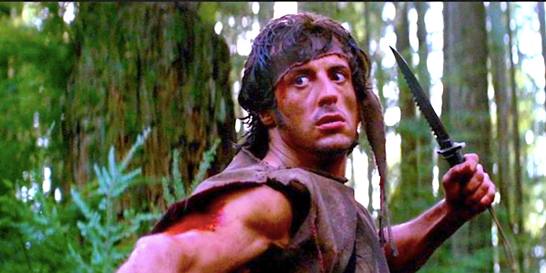 Sylvester Stallone as John Rambo holds a knife in the forest in a scene from Rambo: First Blood.