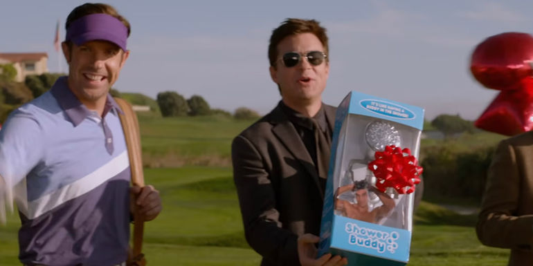 Nick (Jason Bateman) holds a Shower Buddy box with a bow on it while standing next to Kurt (Jason Sudeikis) on a golf course in Horrible Bosses 2.