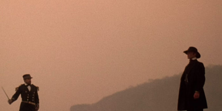 Ed Harris' Walker standing on a beach looking at an army officer in Walker 1987