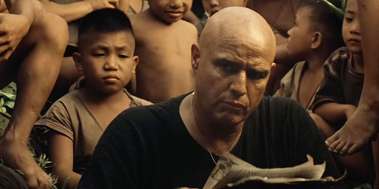 Marlon Brando as Kurtz looking up from his paper while surrounded by Vietnamese children In Apocalypse Now.