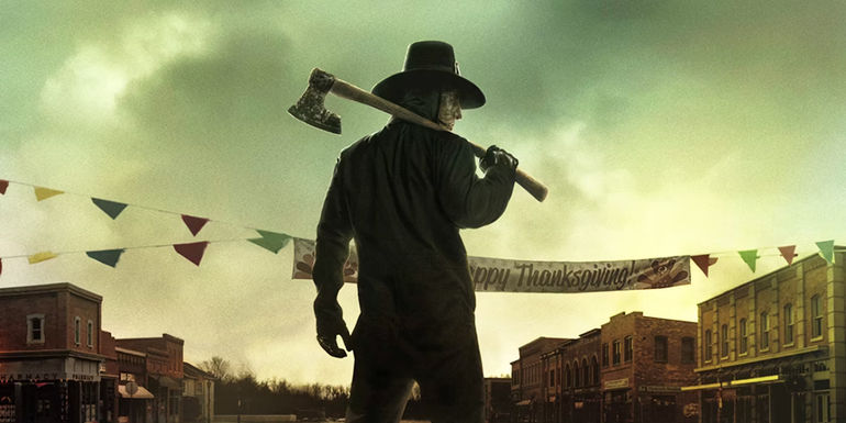 A hat-wearing figure stands in the middle of a small-town street with an axe held over his shoulder on the poster for Thanksgiving
