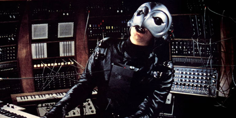 The Phantom (William Finley) plays music in room filled with soundboards in Phantom of the Paradise.