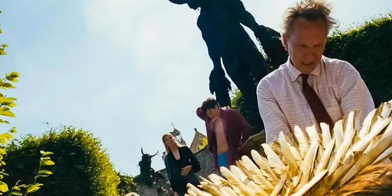 James Catton is kneeling before his dead son who is wearing wings. The Catton family and Oliver stand back by the statue of the Minotaur looking at the scene in Saltburn.