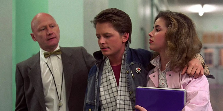 Marty with his arm around Jennifer as Mr. Strickland talks to him in the hallway in Back to the Future
