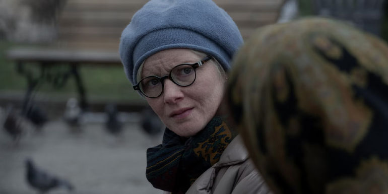 Margo and a mysterious woman in a shawl meet in a public park