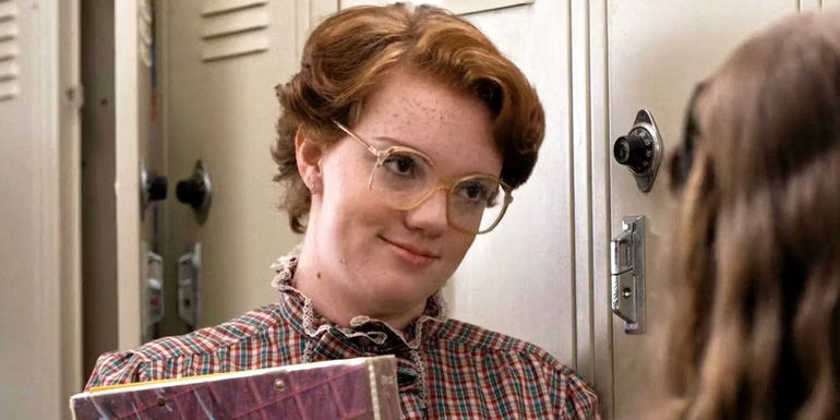 Barb (Shannon Purser) leaning against some lockers and talking to Nancy on Stranger Things.