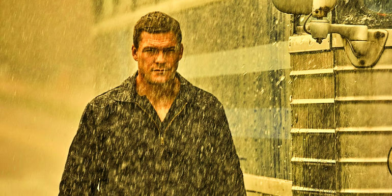 Alan Ritchson as Jack Reacher walking beside bus in the rain in Reacher season 1