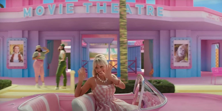 Margot Robbie as Stereotypical Barbie drives past a movie theater with Wizard of Oz posters in Barbie